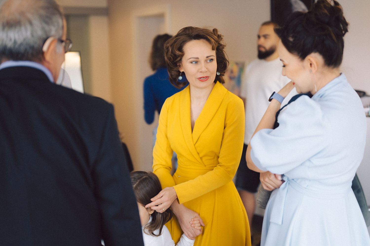 Group of people in formal attire gathered for conversation in bright indoor setting.