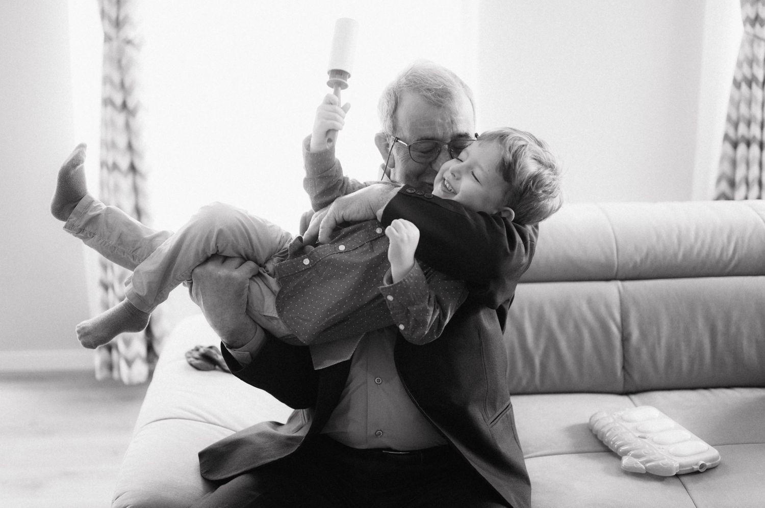 Black and white photo of playful interaction between older man and child on couch.