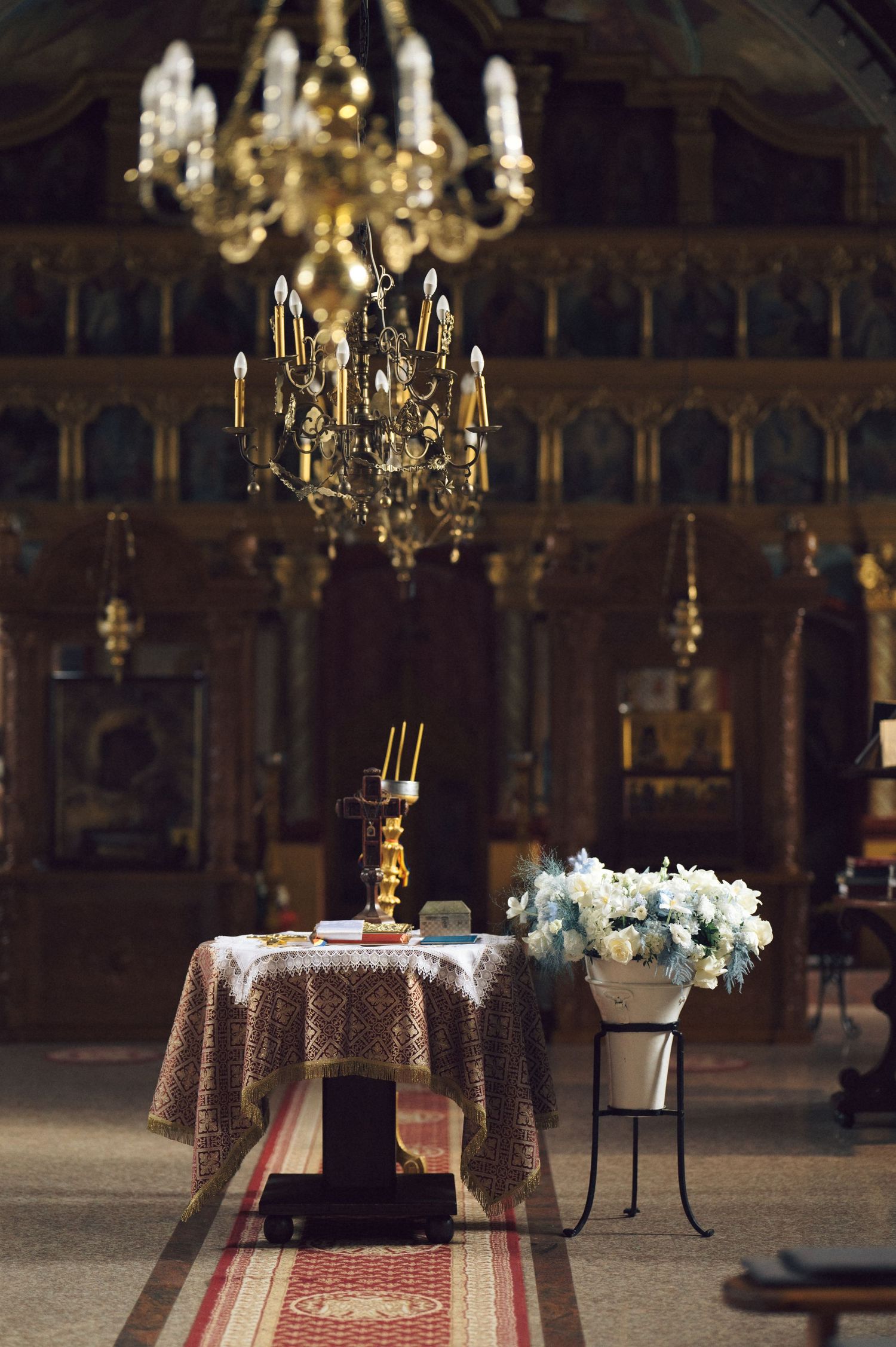 Elegant church interior with crystal chandeliers and a table draped with lace cloth holding white floral arrangements.