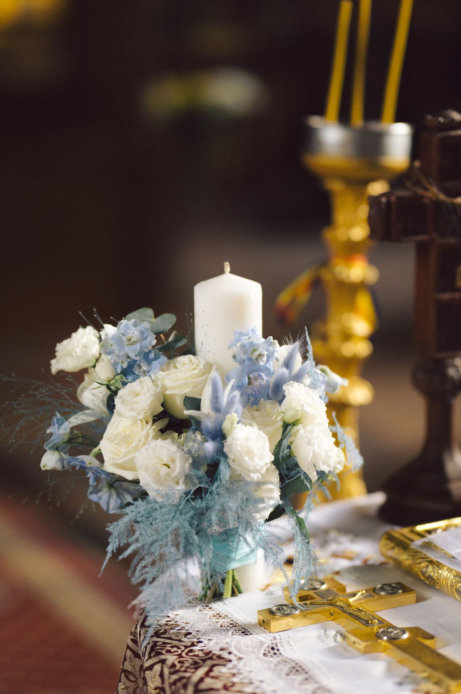 White and blue floral arrangement with candle on lace-covered table during religious ceremony.