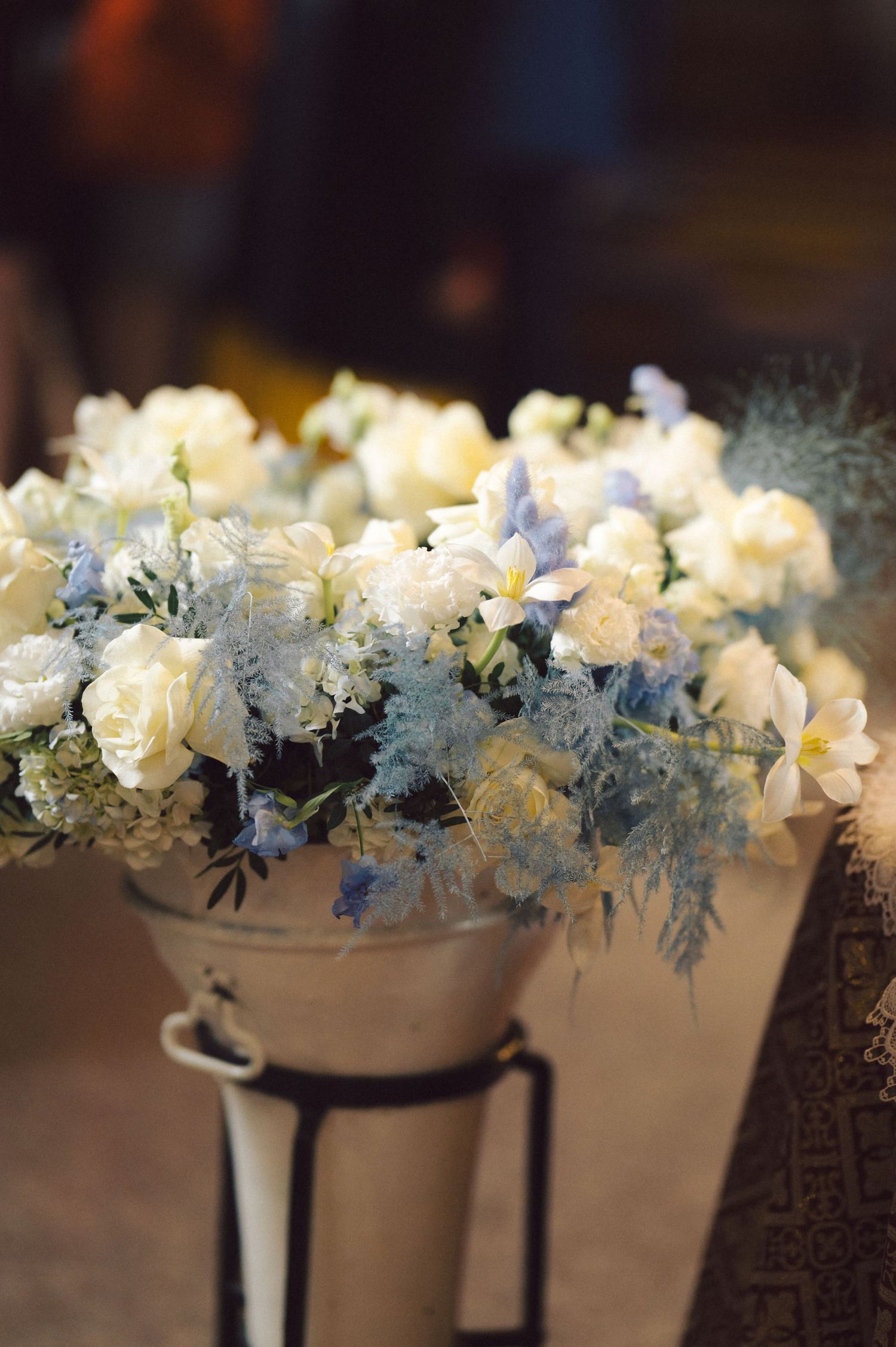 Delicate arrangement of white roses and blue flowers in a metallic stand.