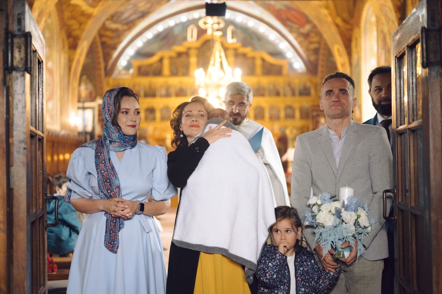 Religious ceremony participants gathered in ornate church corridor with golden iconostasis.