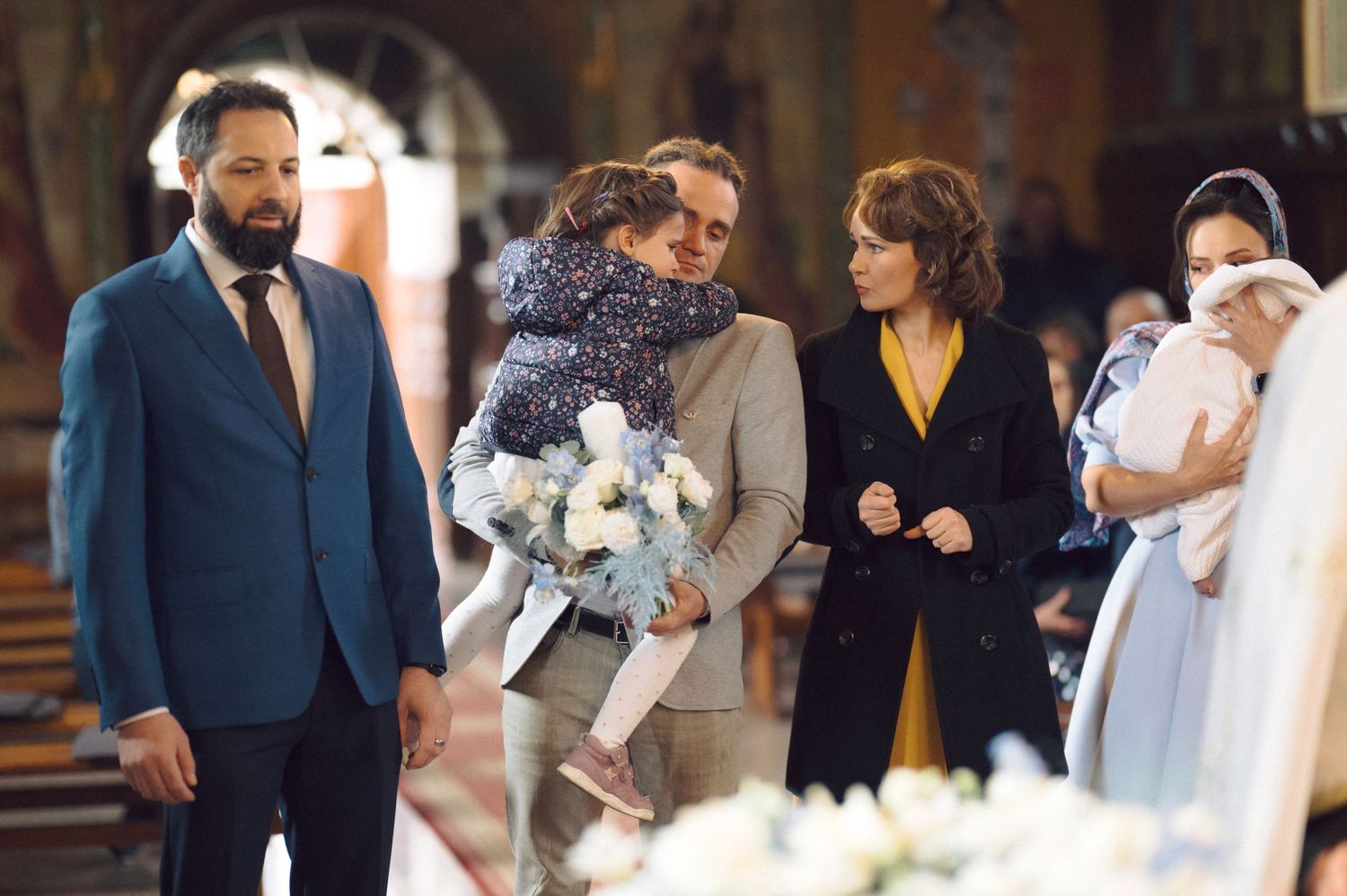 Family gathering during a church ceremony with formal attire and white floral bouquets.