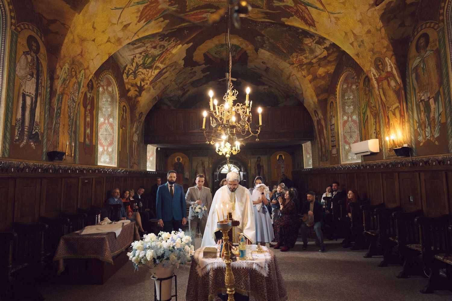 Orthodox church ceremony in an ornate hall with painted ceiling and chandelier.