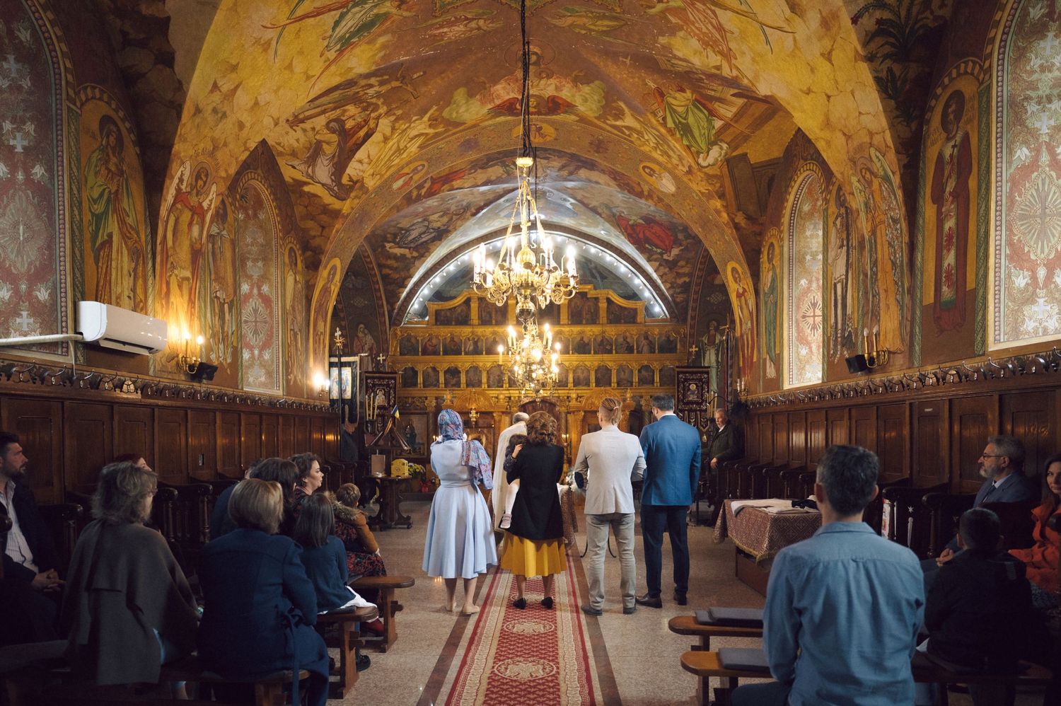 Wedding ceremony in progress inside a beautiful Orthodox church with decorated vaulted ceilings.