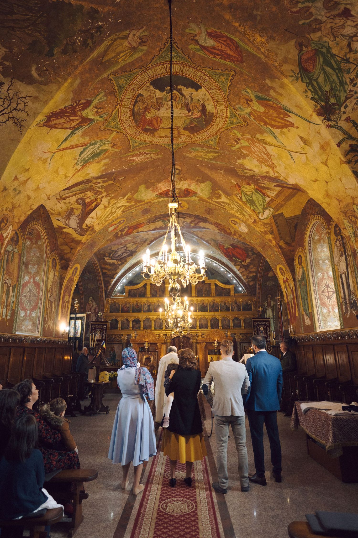 Stunning Byzantine-style church interior with golden frescoes and crystal chandelier during ceremony.