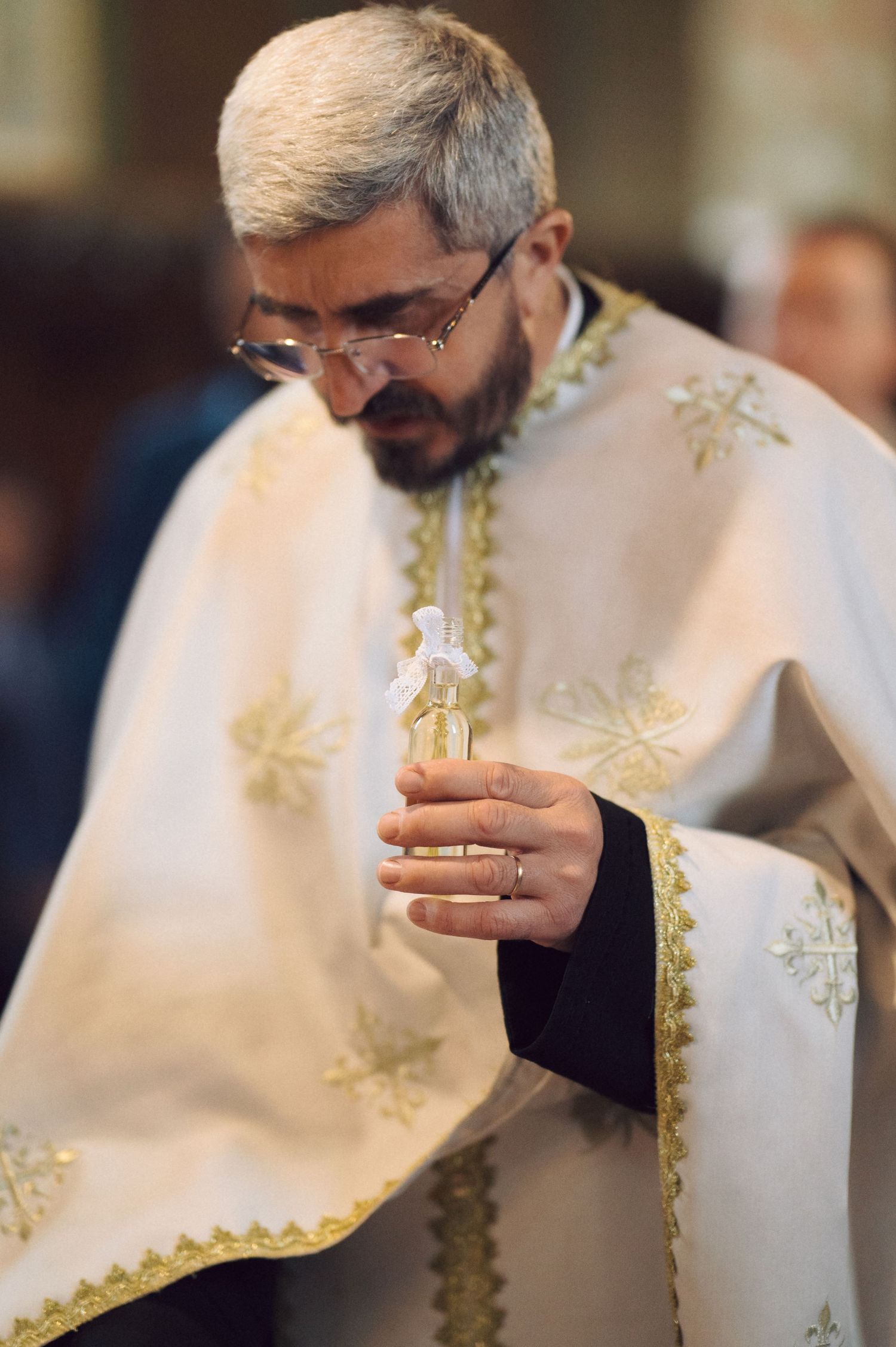 Orthodox priest in white embroidered vestments holding a small ceremonial object.