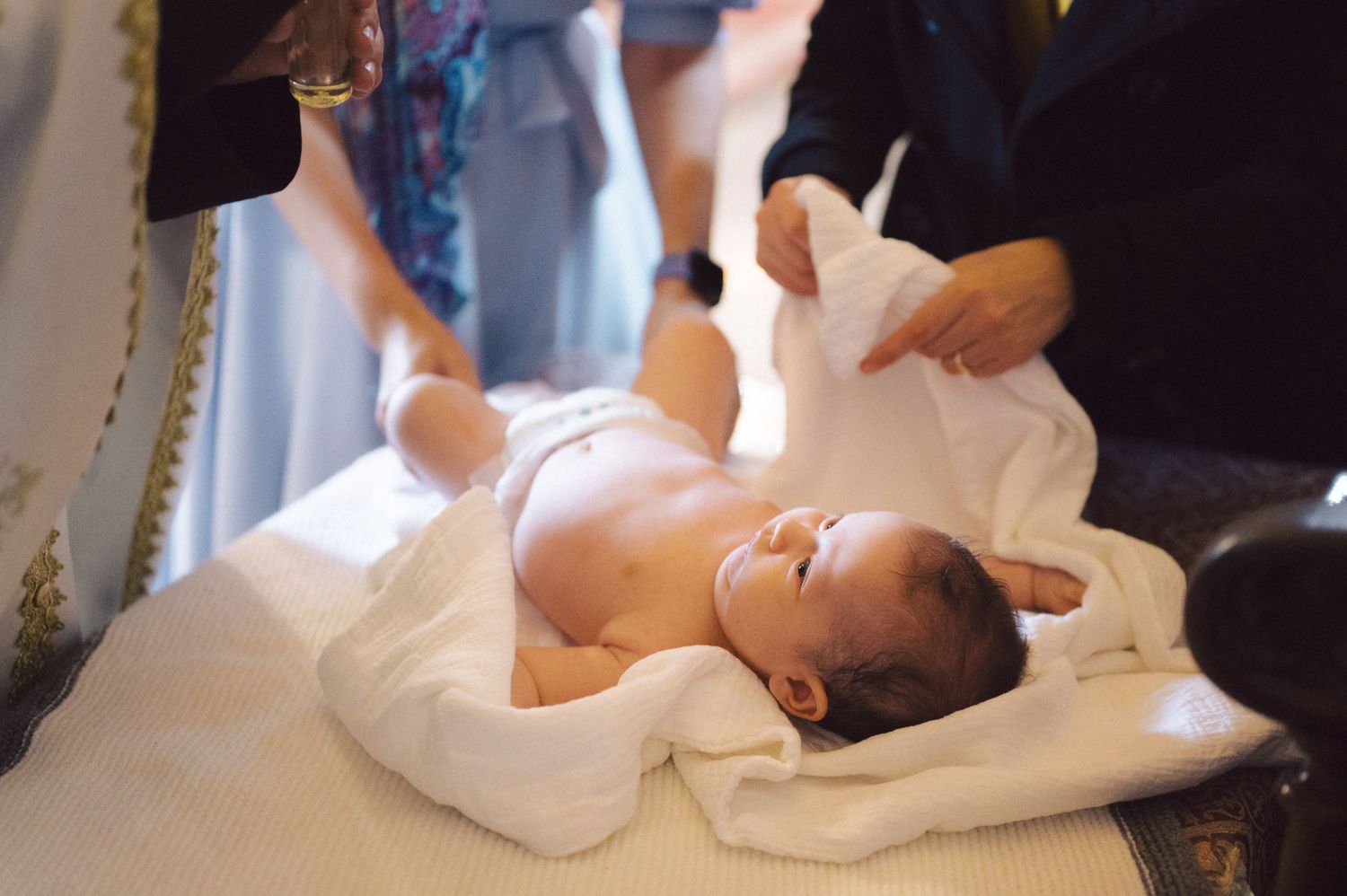 Baby in white baptismal gown during Orthodox christening ceremony.
