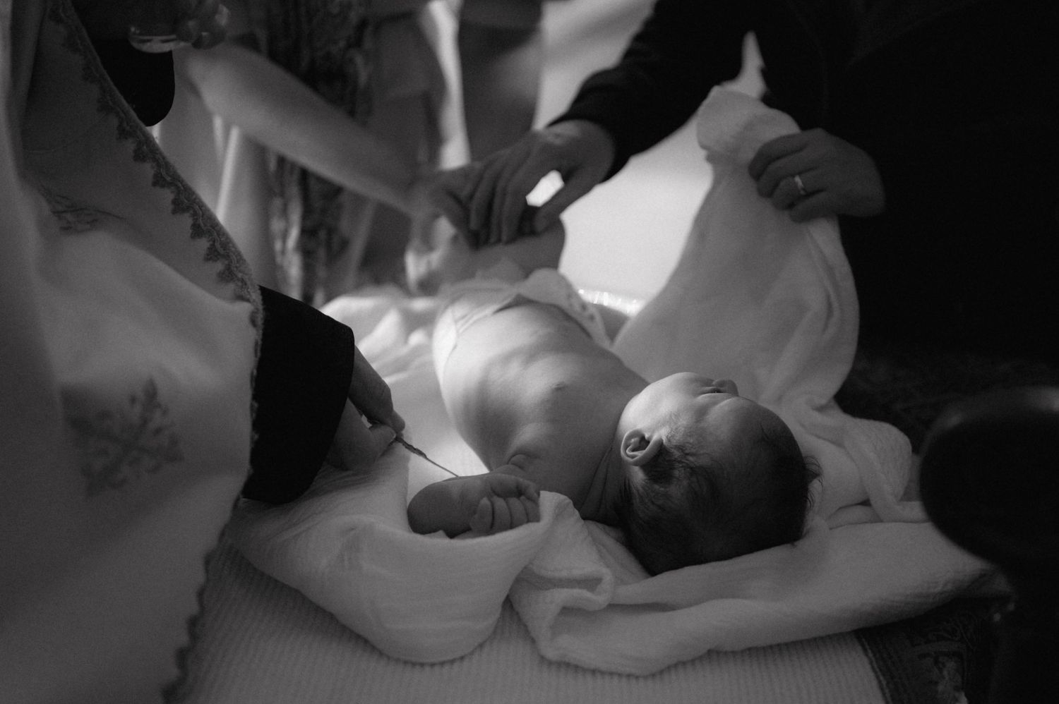 Black and white photo of infant baptism ceremony with priests performing ritual.