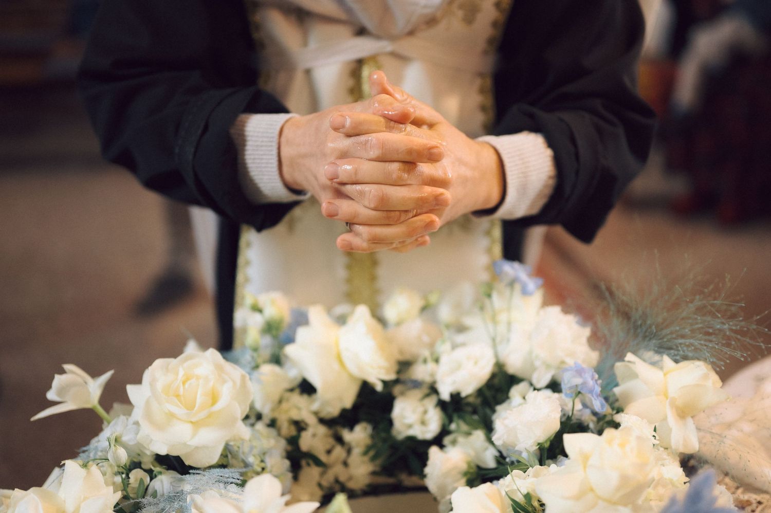 Clasped hands next to elegant white rose and blue flower arrangement.