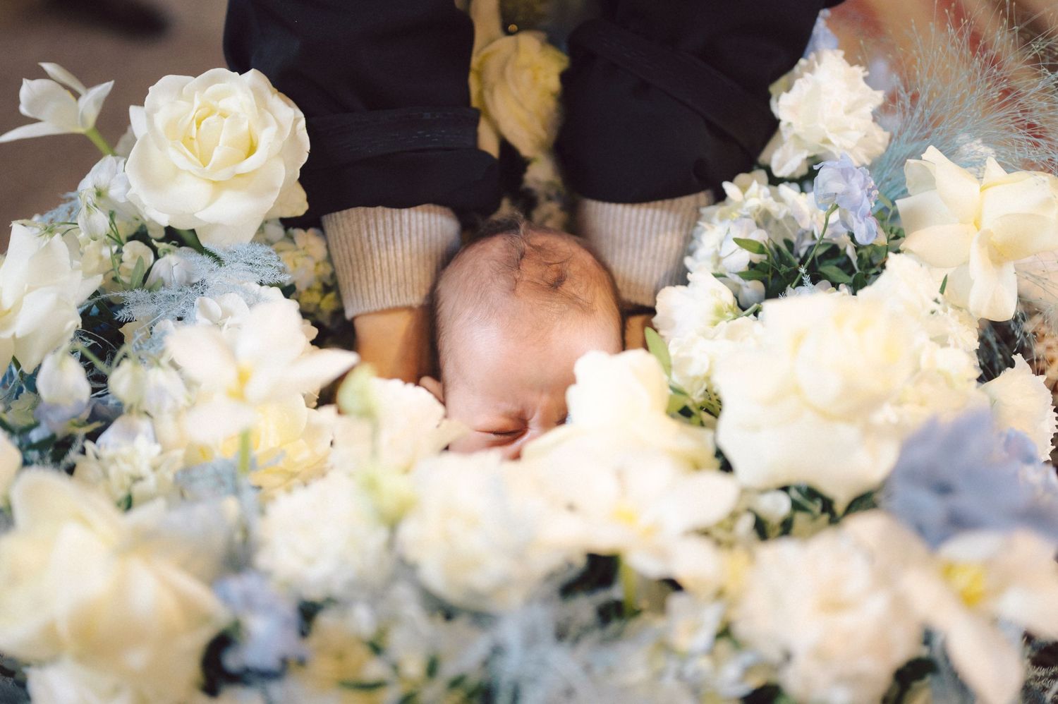 Close-up of an infant surrounded by white and blue roses during a religious ceremony.