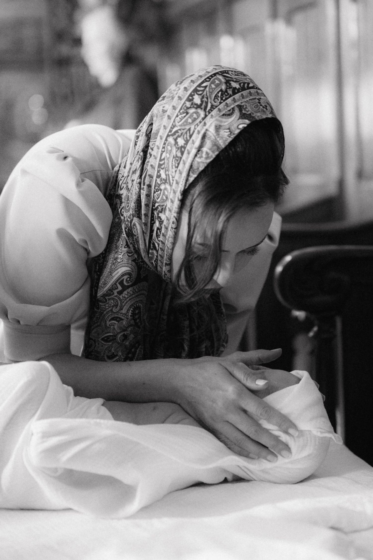 Woman in headscarf carefully preparing white fabric in black and white photograph.