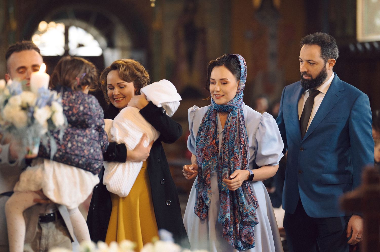 Orthodox christening ceremony with floral decorations and gathered family members.