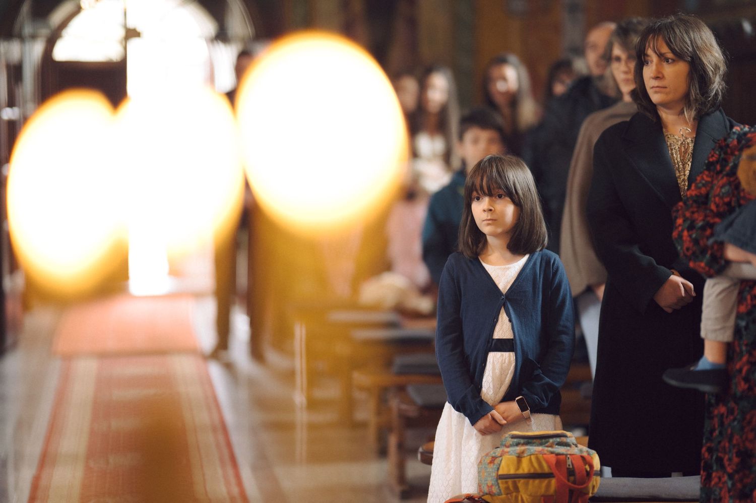 Church interior with glowing candles in foreground and attendees in the background.