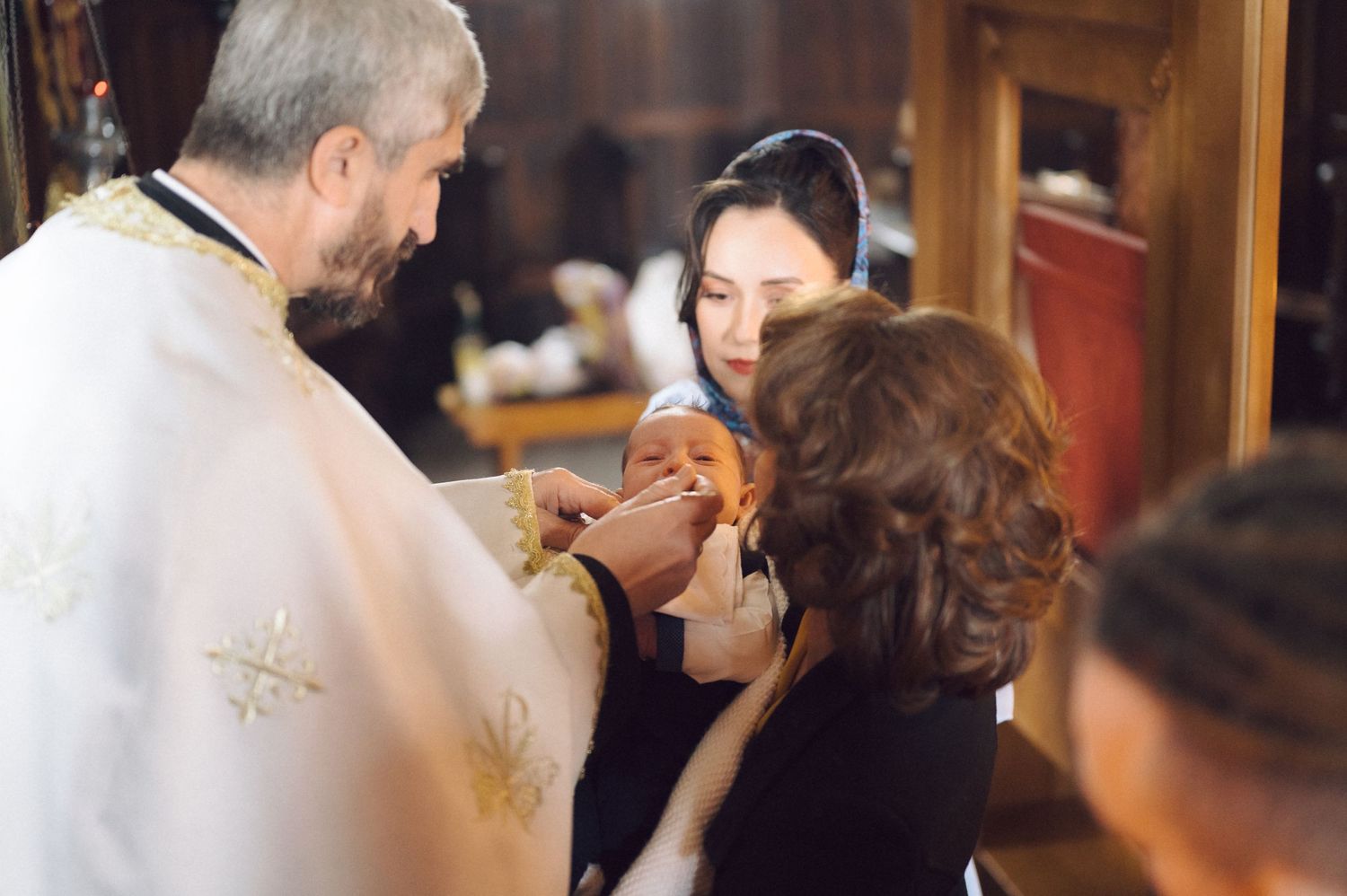 A candlelit baptism ceremony shows a priest performing religious rites with attendees.