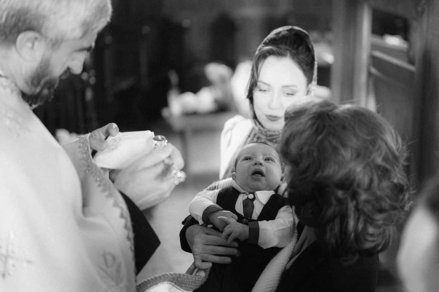 An intimate baptism ceremony takes place with attendees gathered around a small infant.