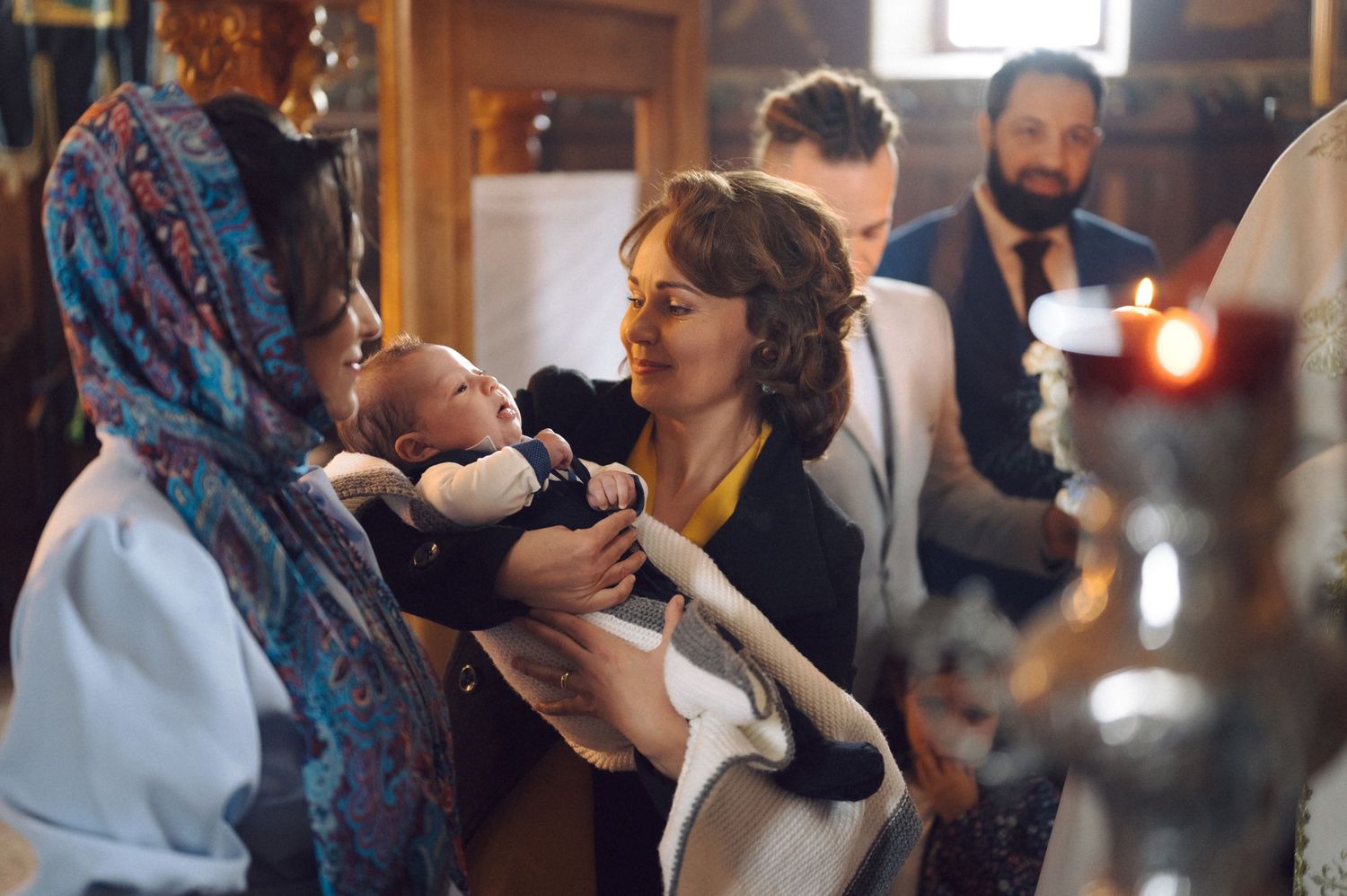 A group gathers around a small infant during a traditional religious ceremony in a church.