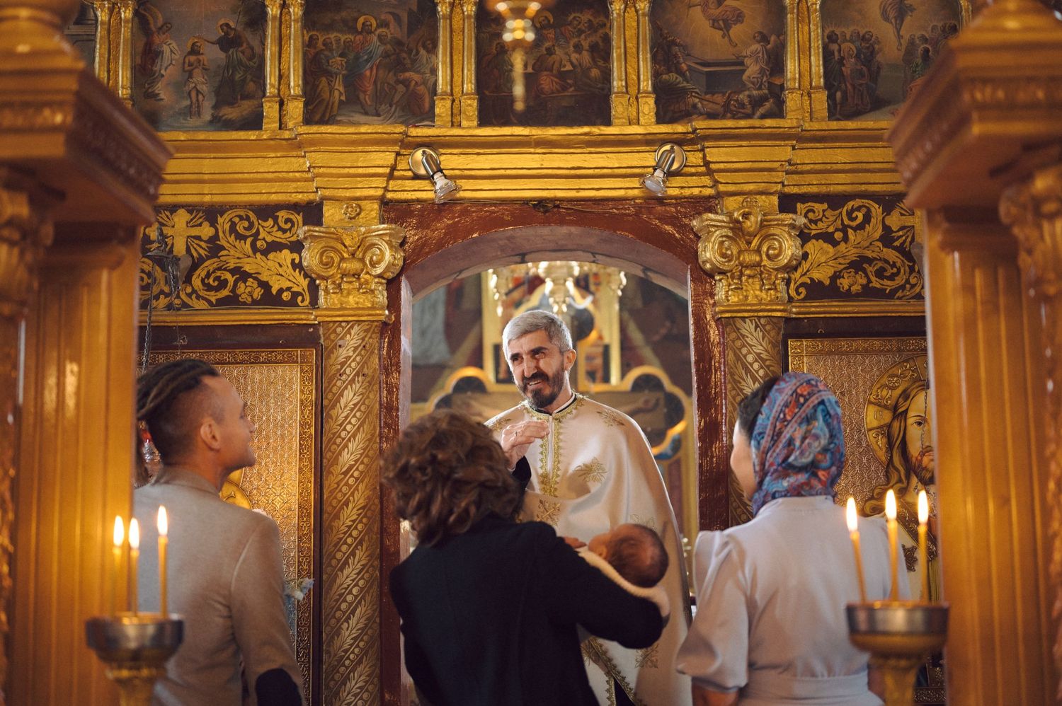 Orthodox religious ceremony taking place in ornate church with gilded decorations and candlelight.