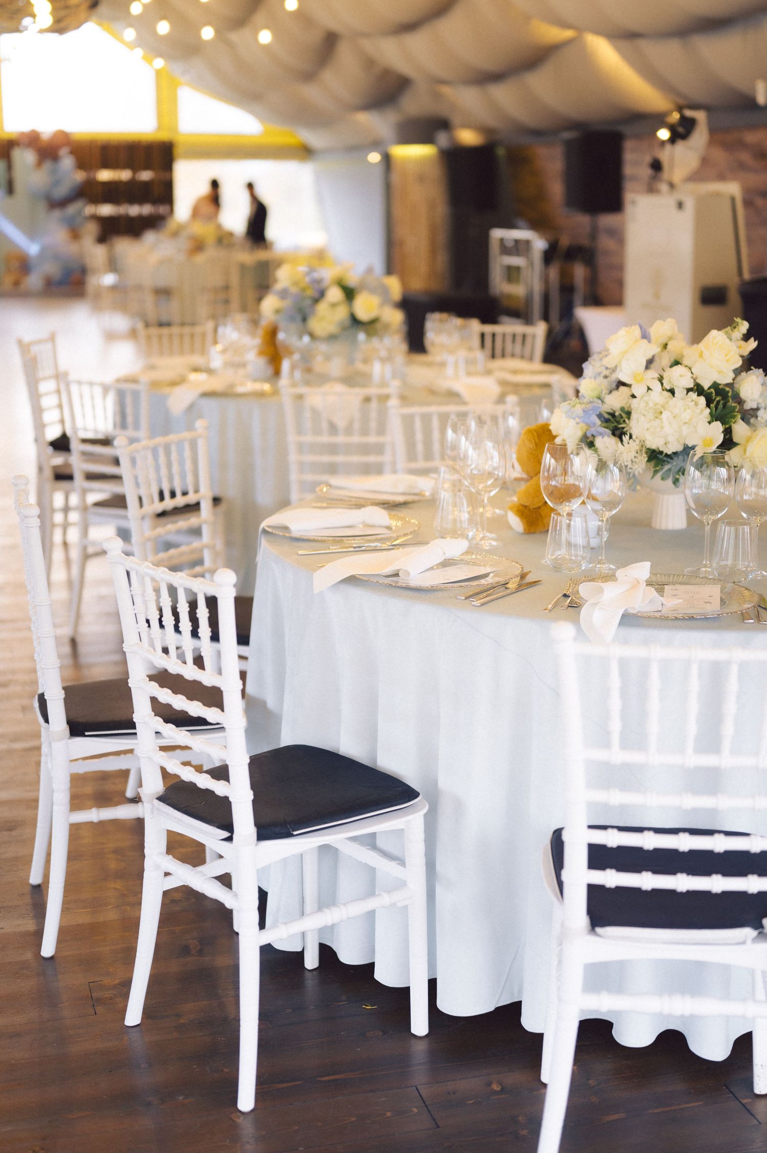 White chiavari chairs around circular tables with floral centerpieces at wedding reception.