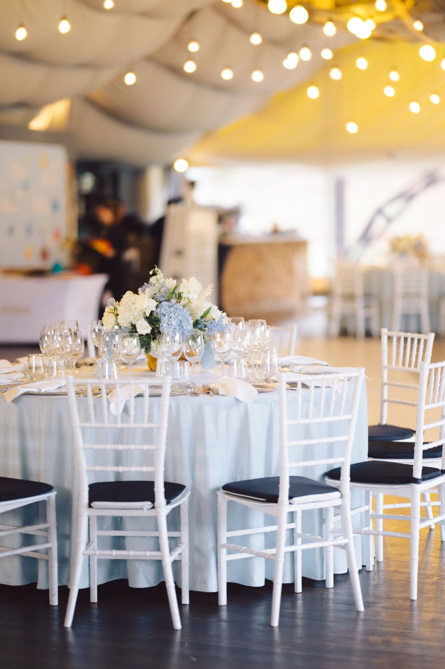 Wedding reception tables with white linens and chiavari chairs under string lights.