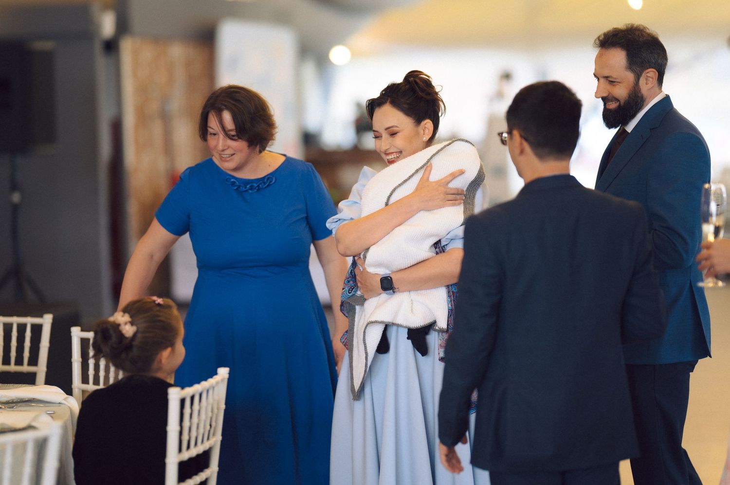 Wedding guests gathering around tables at indoor reception venue.