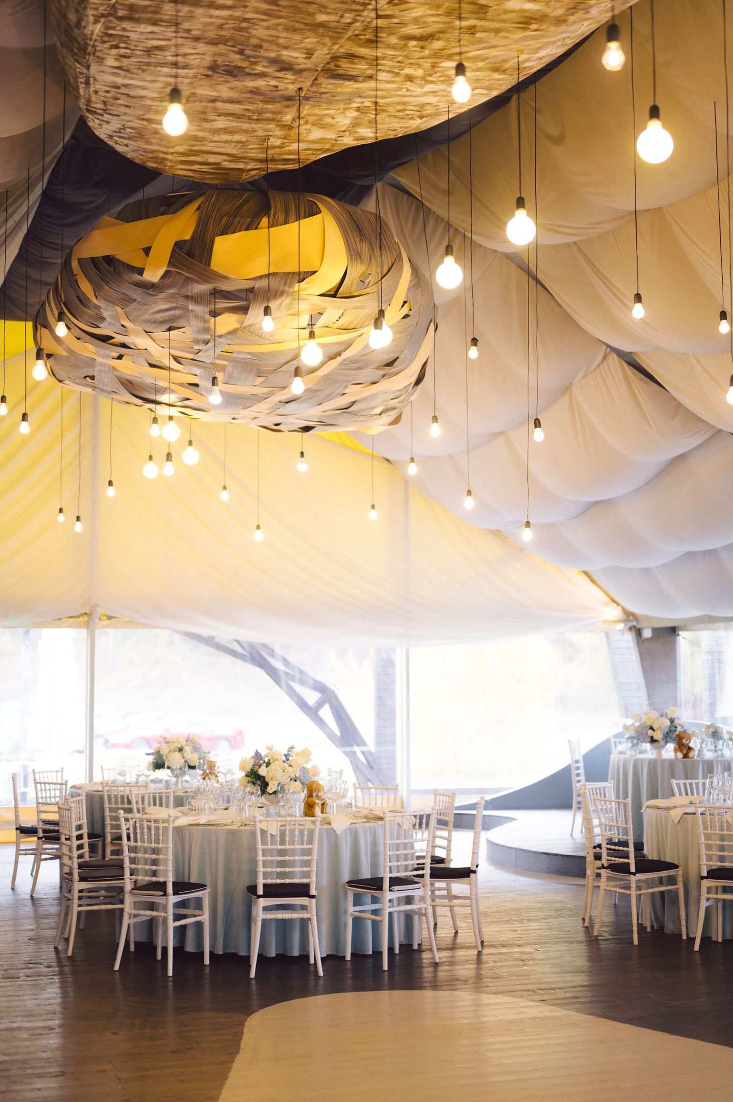 Elegant wedding reception venue with draped fabric ceiling, hanging lights and round tables.