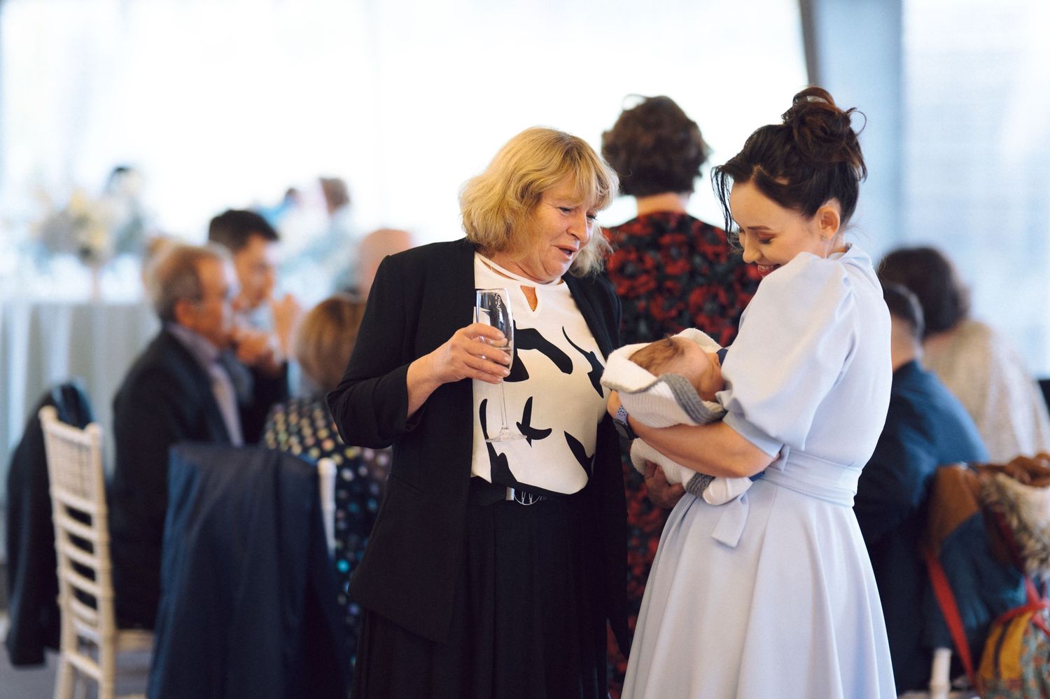 Reception guests gather around elegant white-clothed tables under tent.