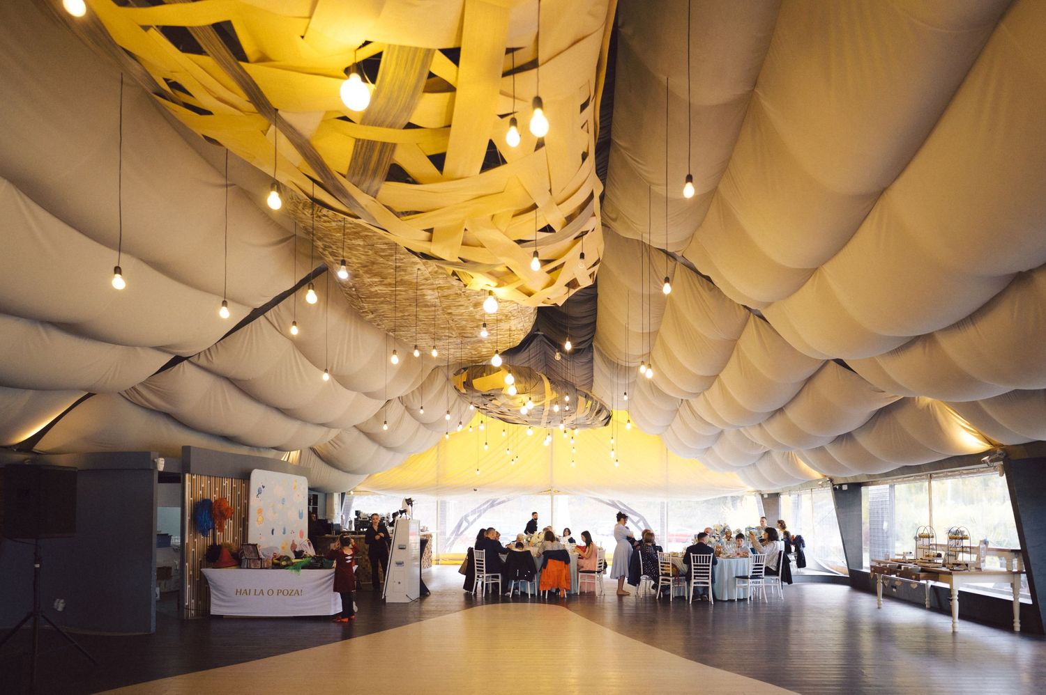 Modern event space with yellow geometric ceiling decor and white draping.