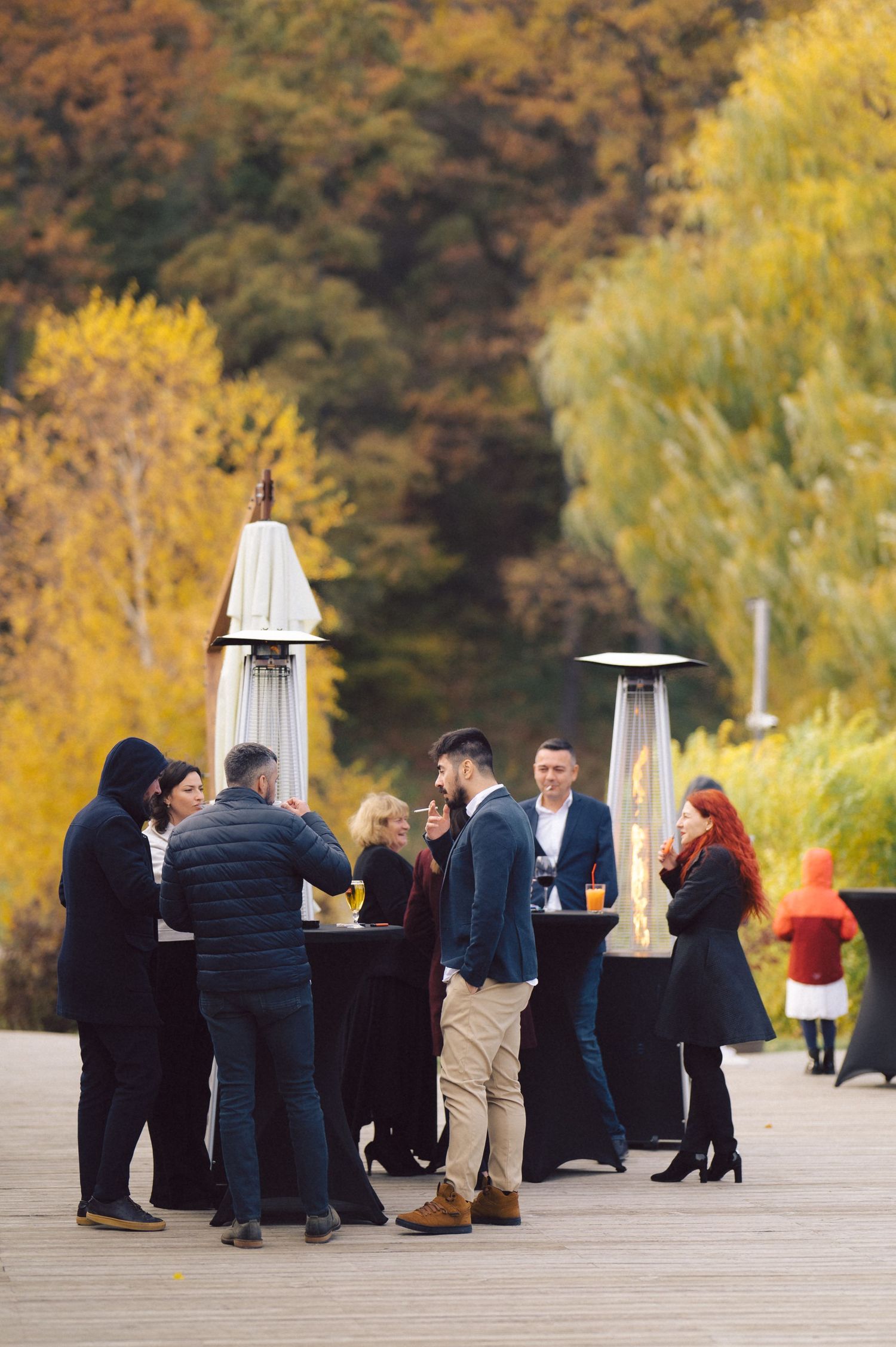 Outdoor gathering around cocktail tables with heaters during autumn.