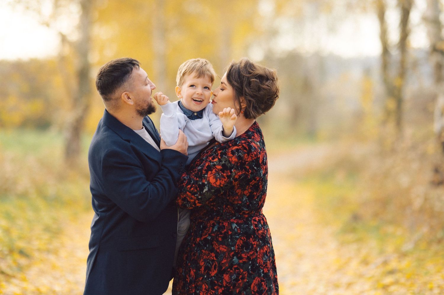 A family shares a tender moment together in an autumn setting with golden leaves in the background.