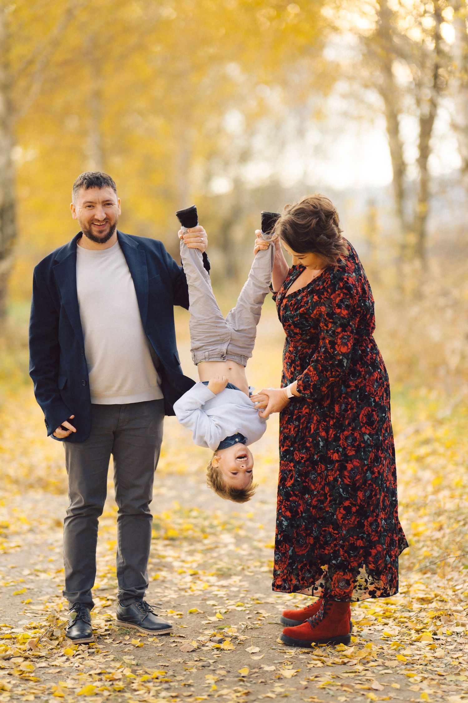 Playful family moment in autumn forest as they hold their little one upside down.