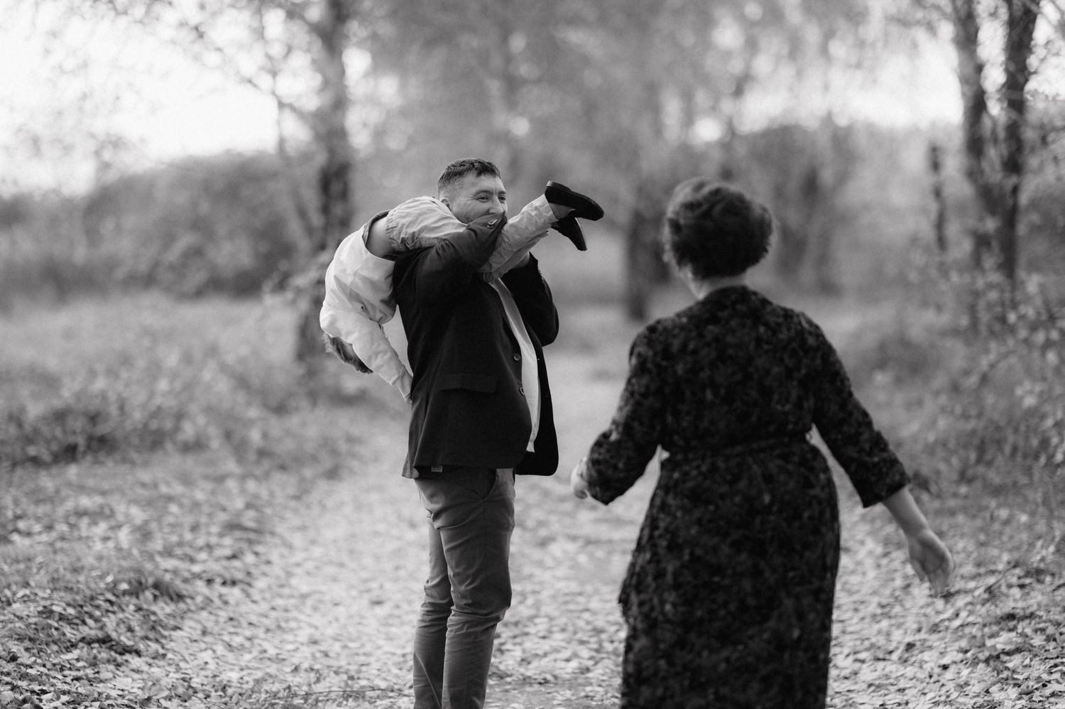 Black and white photo capturing a playful family moment on a forest path.