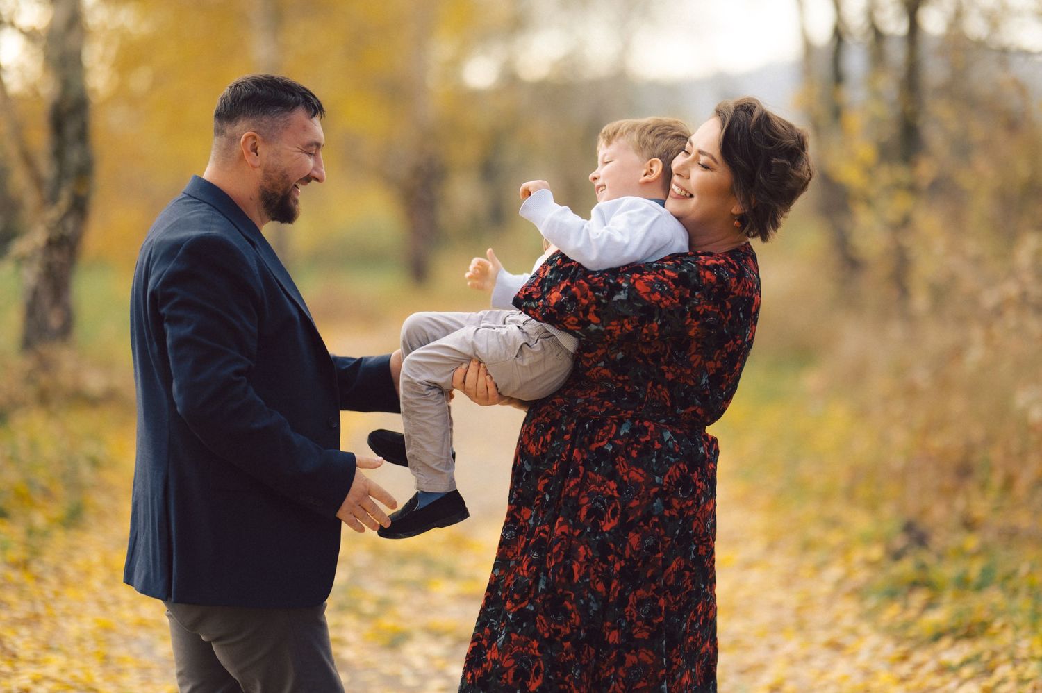 Family laughing and playing together surrounded by golden fall foliage.
