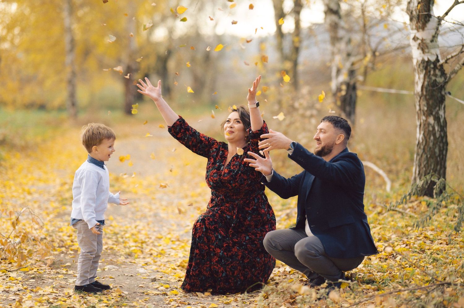 Family playing with falling autumn leaves in a forest with golden foliage.