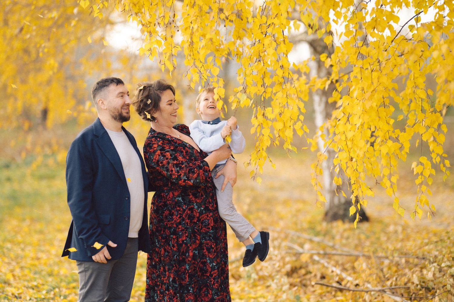 Family enjoying a moment together beneath golden autumn tree branches.