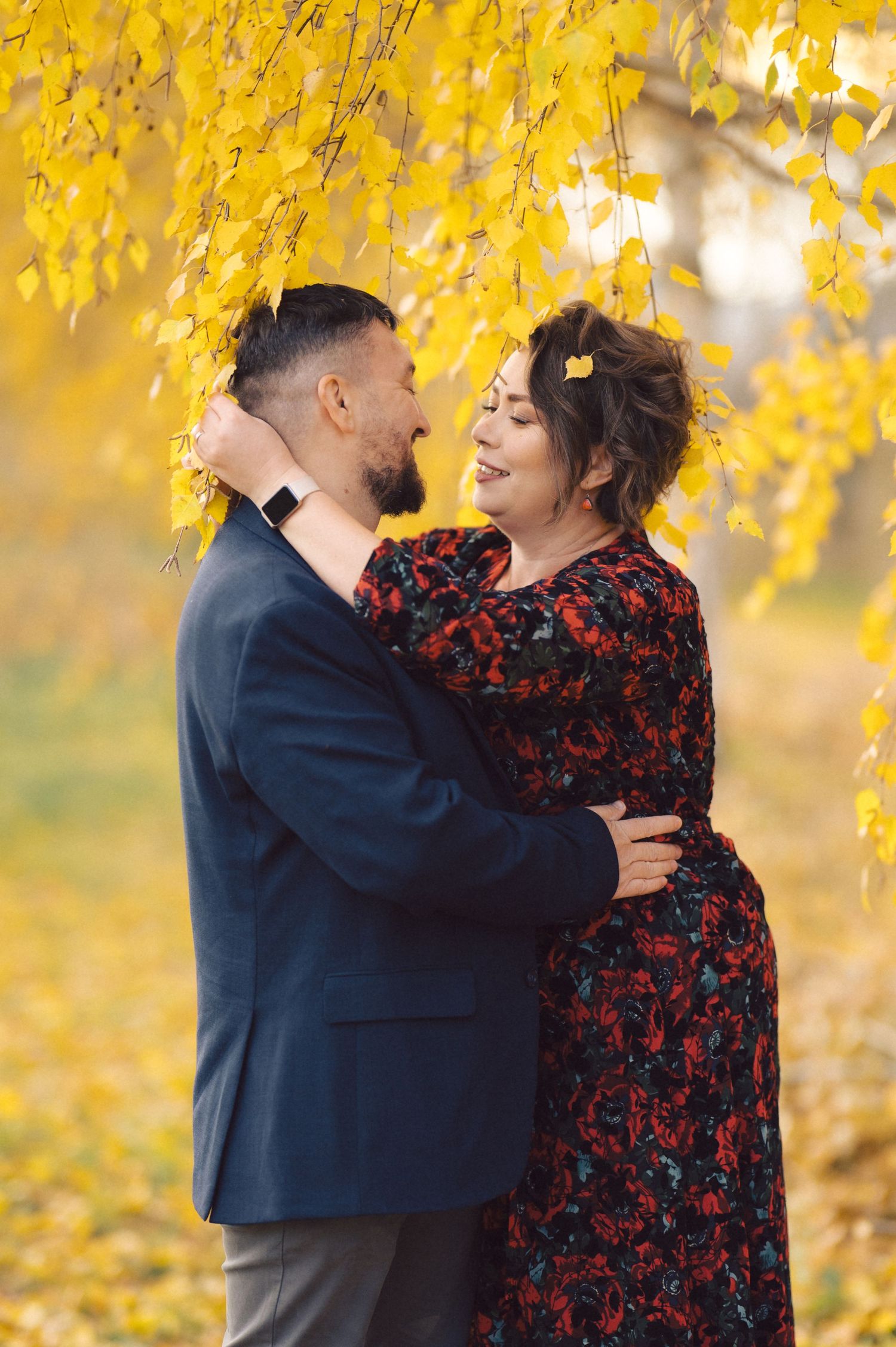 Romantic couple embracing under yellow autumn leaves in soft lighting.