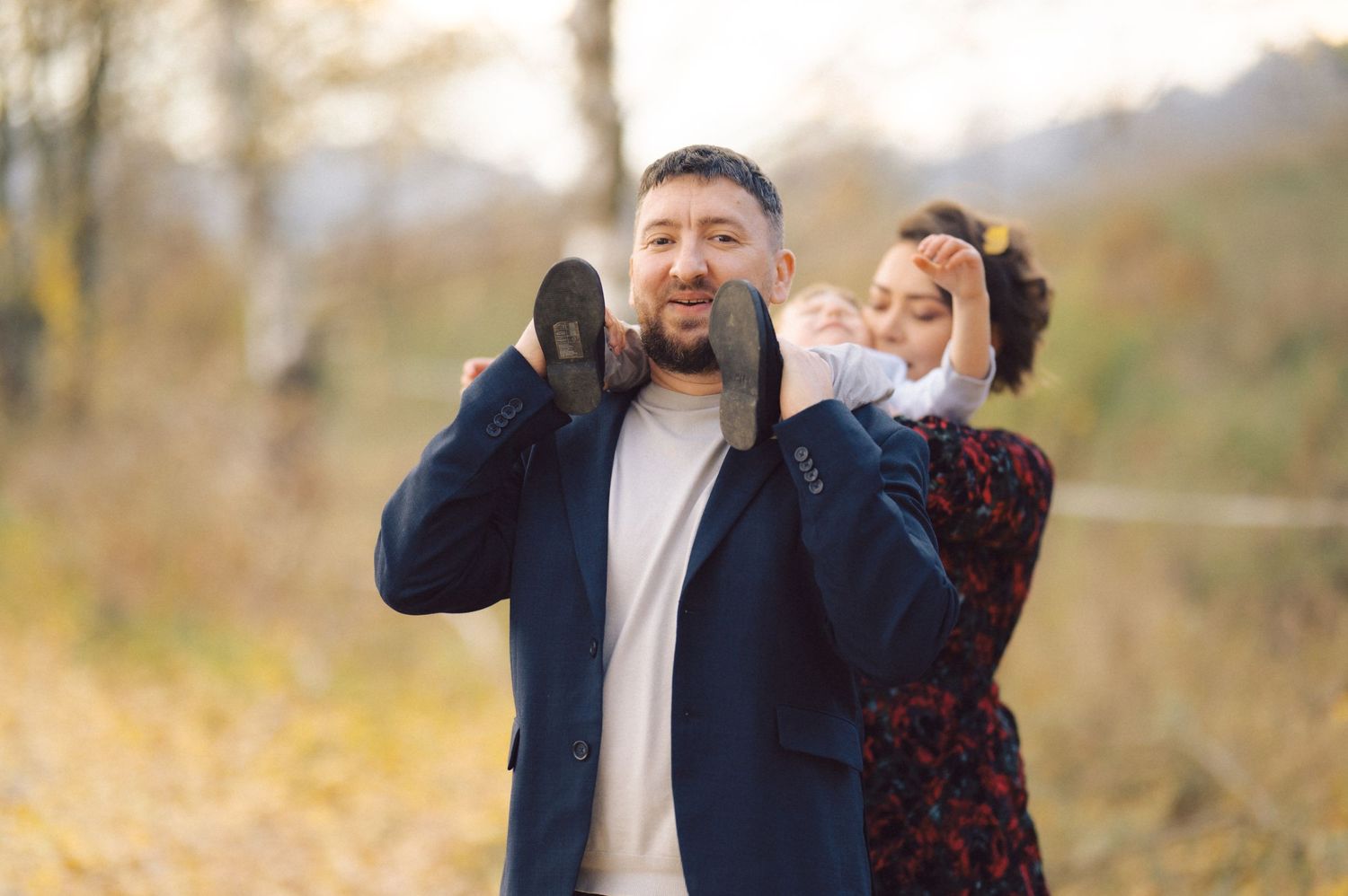 A couple playfully poses together outdoors during autumn with yellow foliage in the background.