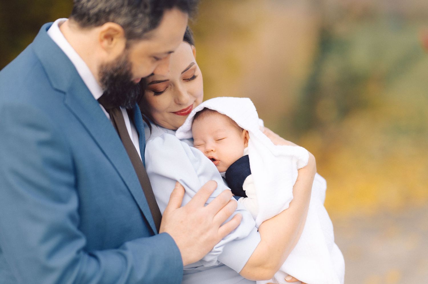 A couple tenderly cradles their newborn baby while surrounded by autumn colors.