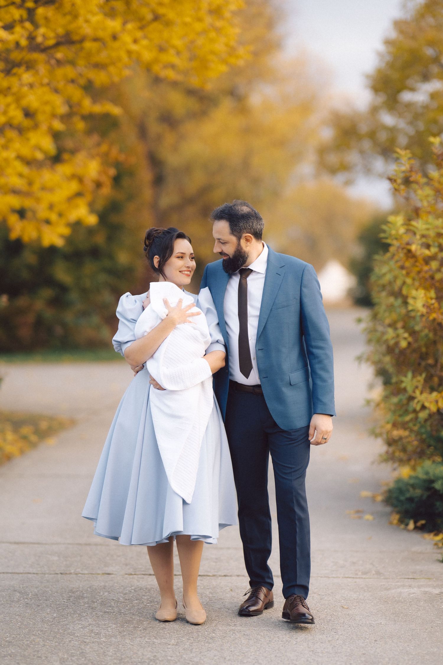 A couple takes a romantic walk together on a path lined with golden autumn trees.