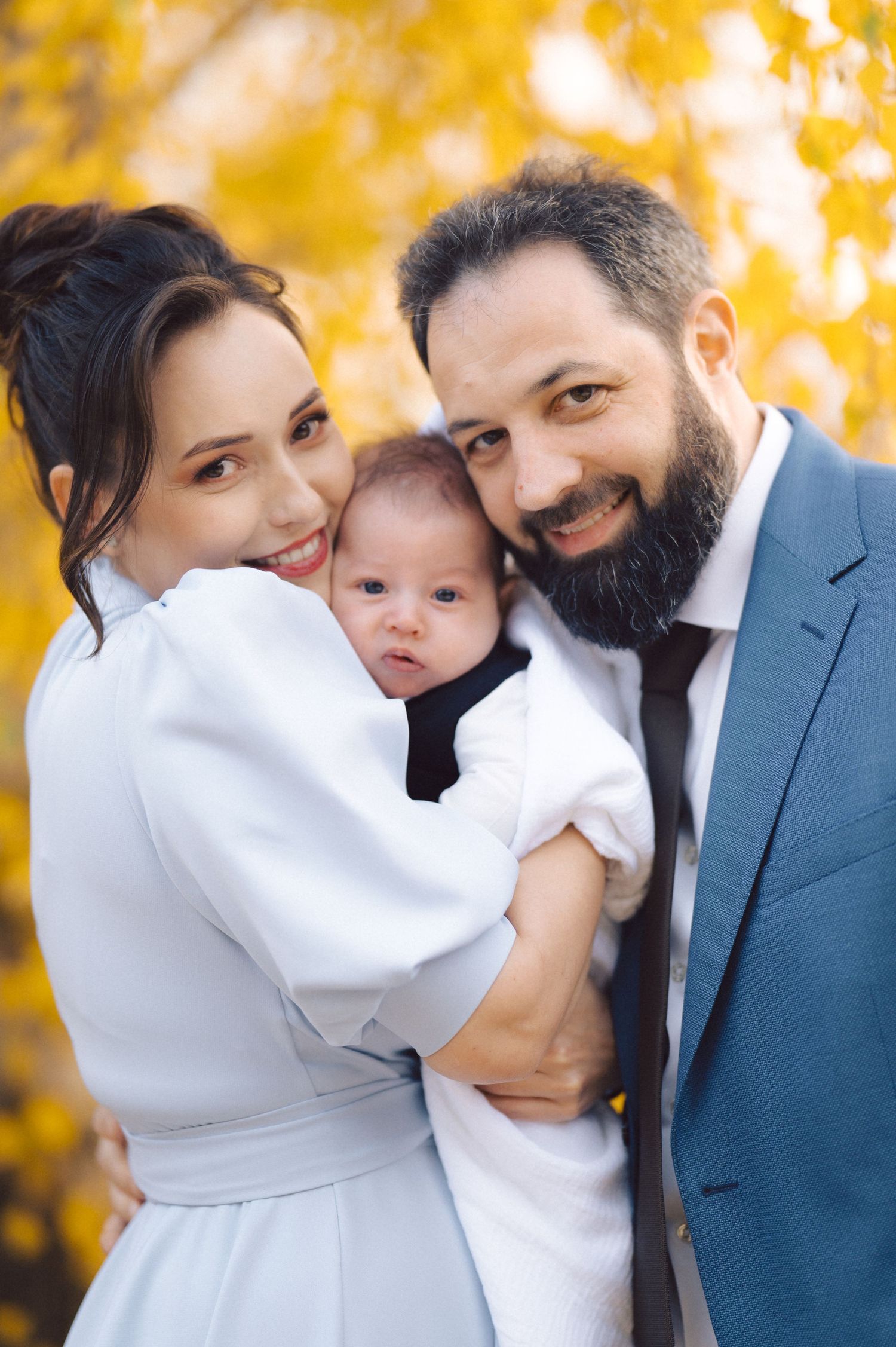 Family portrait with baby between parents against golden fall foliage.
