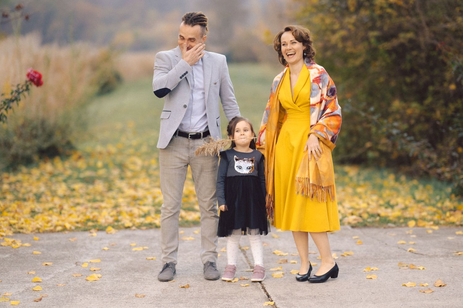 Family walking together on path covered in yellow autumn leaves.