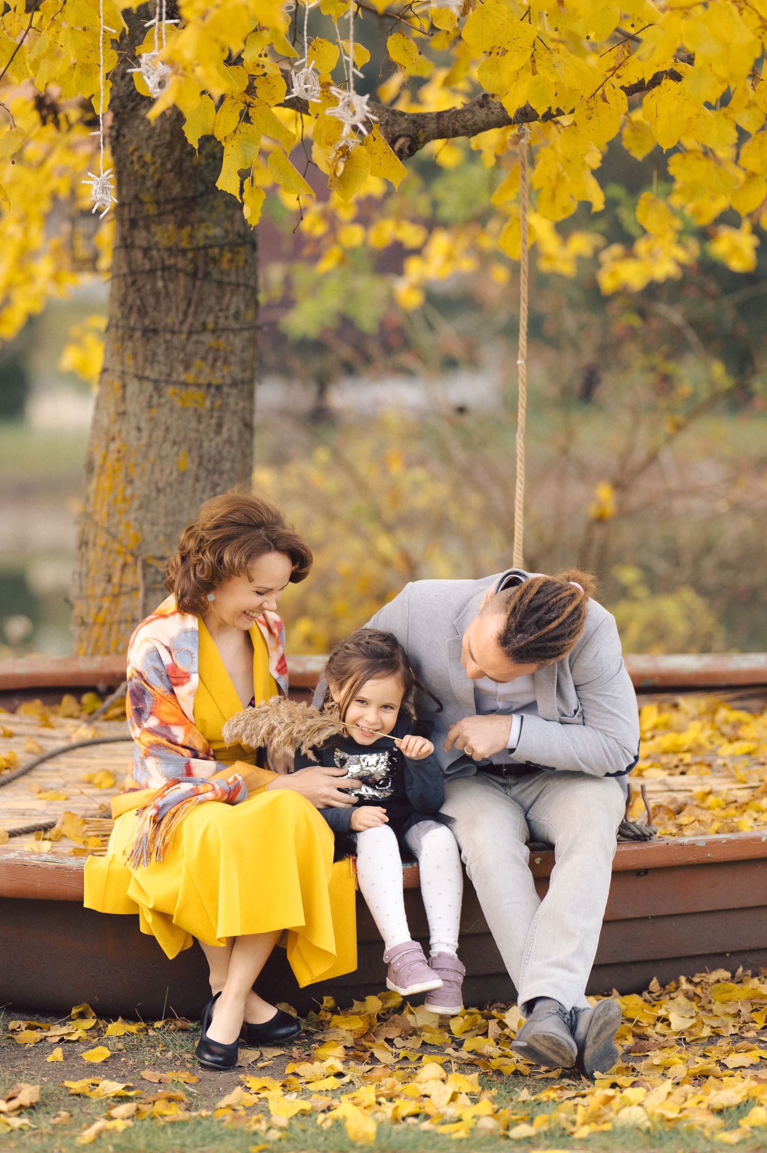 Family sits together on wooden bench under yellow fall foliage sharing an intimate moment.