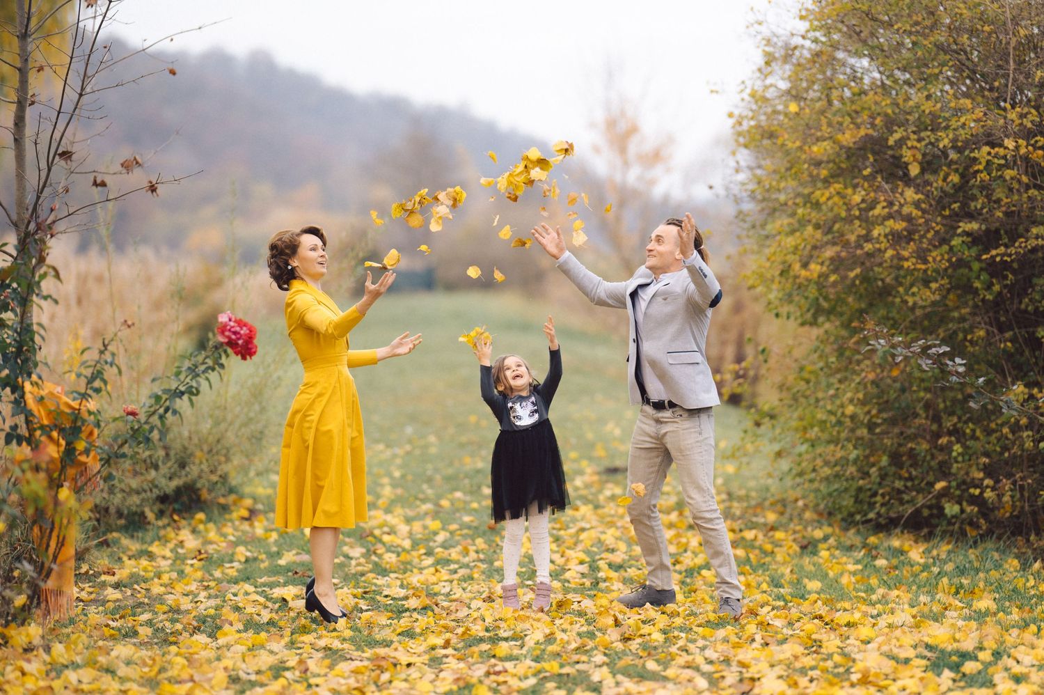 Family throws yellow autumn leaves in the air while playing outdoors on a fall day.