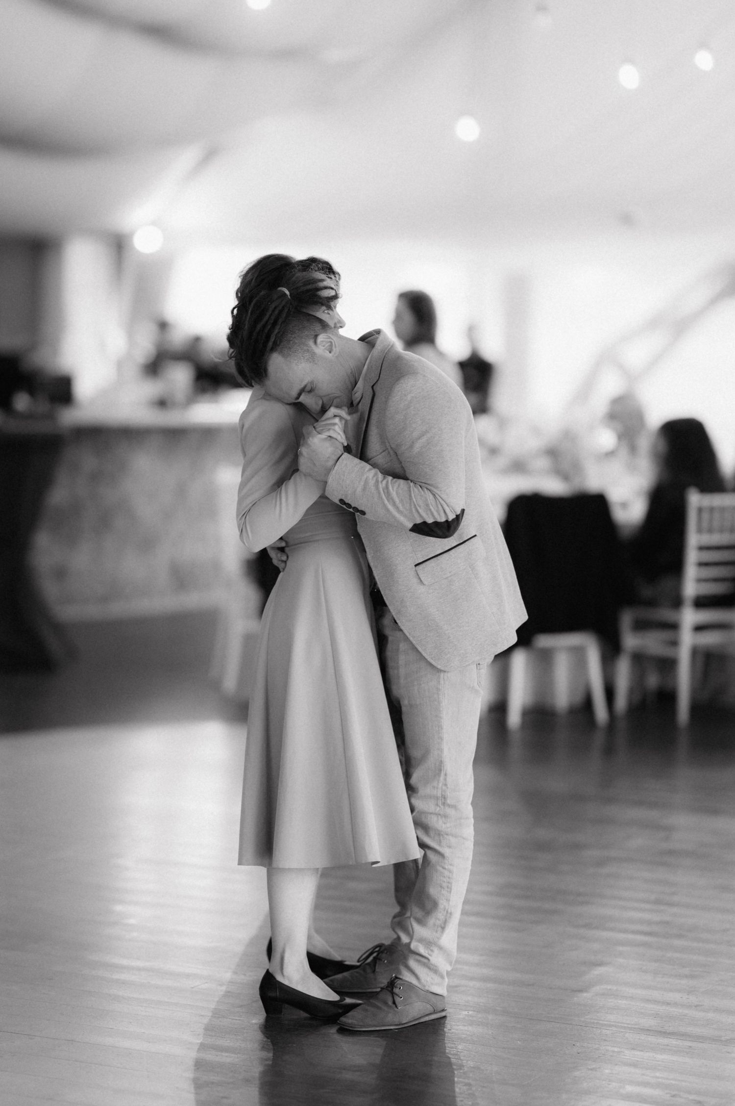 Couple shares intimate embrace while dancing in black and white on indoor dance floor.
