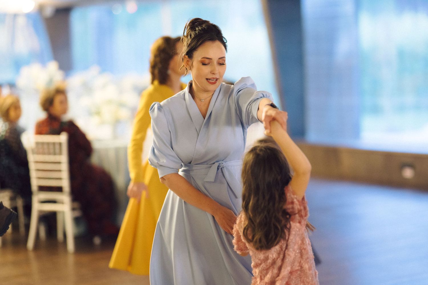 A woman in a gray dress dances with a young child at a celebration.