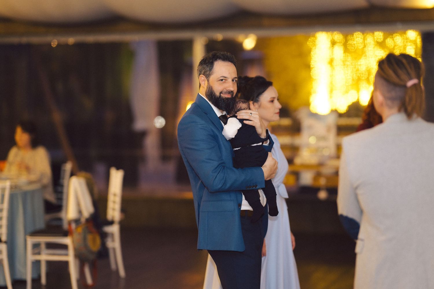 A man in a blue suit holds a small child during an indoor celebration.