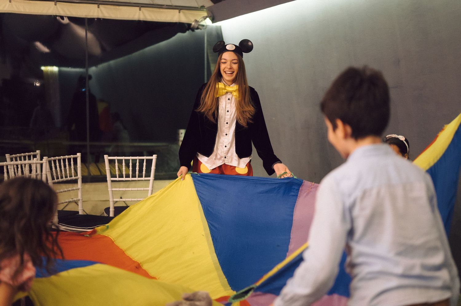 Person in Mickey Mouse ears stands on a colorful parachute during an activity.