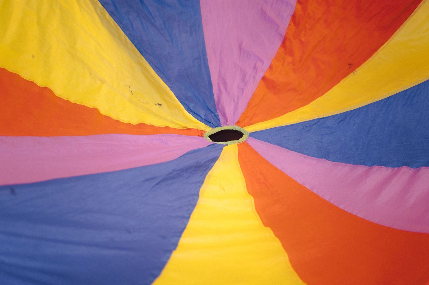 Overhead view of a colorful parachute with radiating stripes in yellow, blue, pink and orange.