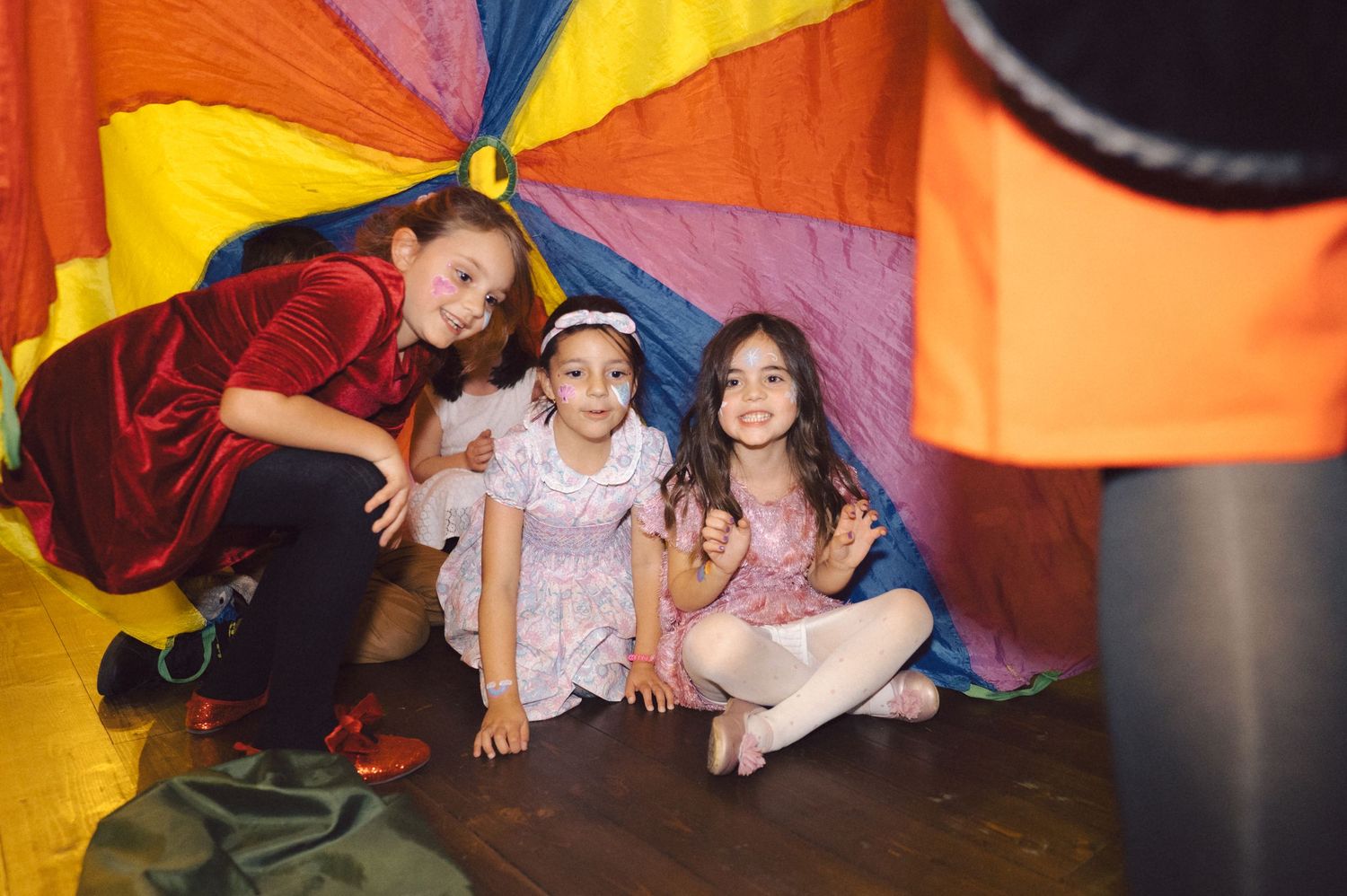 Children playing under a colorful parachute at an indoor event.