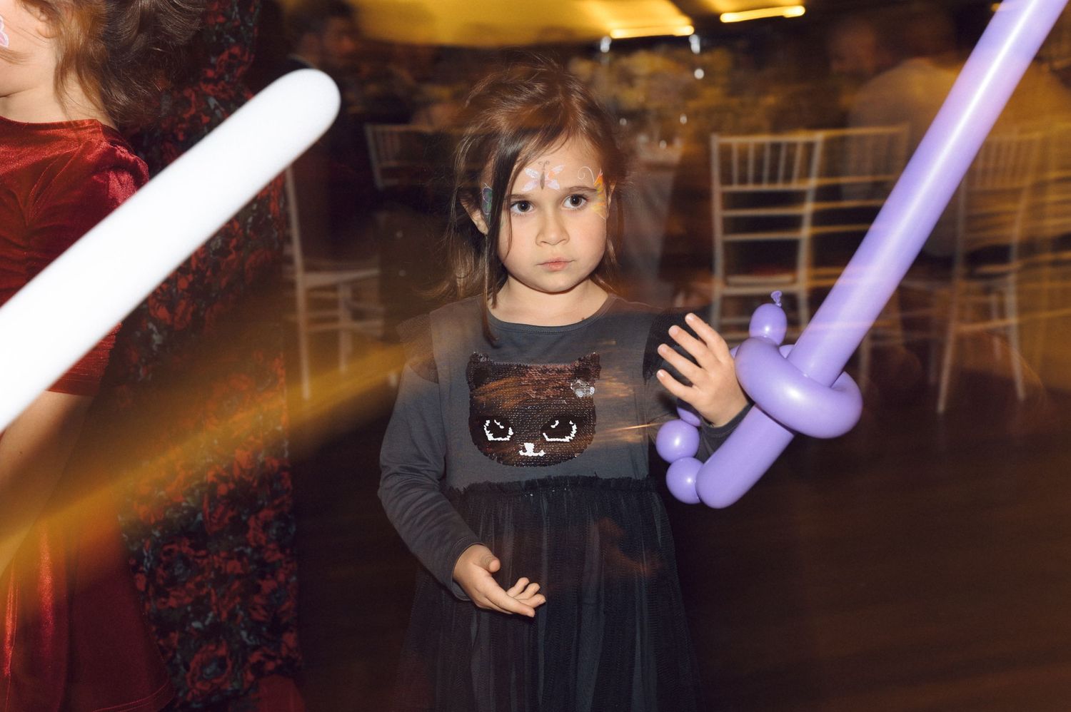Child holds balloon sword toys at indoor party with light effects.